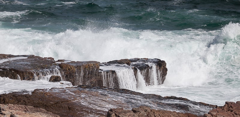 Vom Wasser überschäumende Felsen vor der Küste der Walker Bay