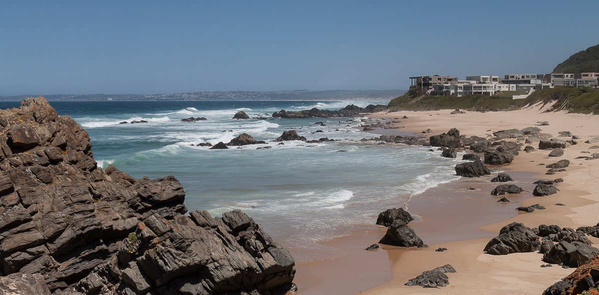 Felsiger Sandstrand mit Plettenberg Bay im Hintergrund